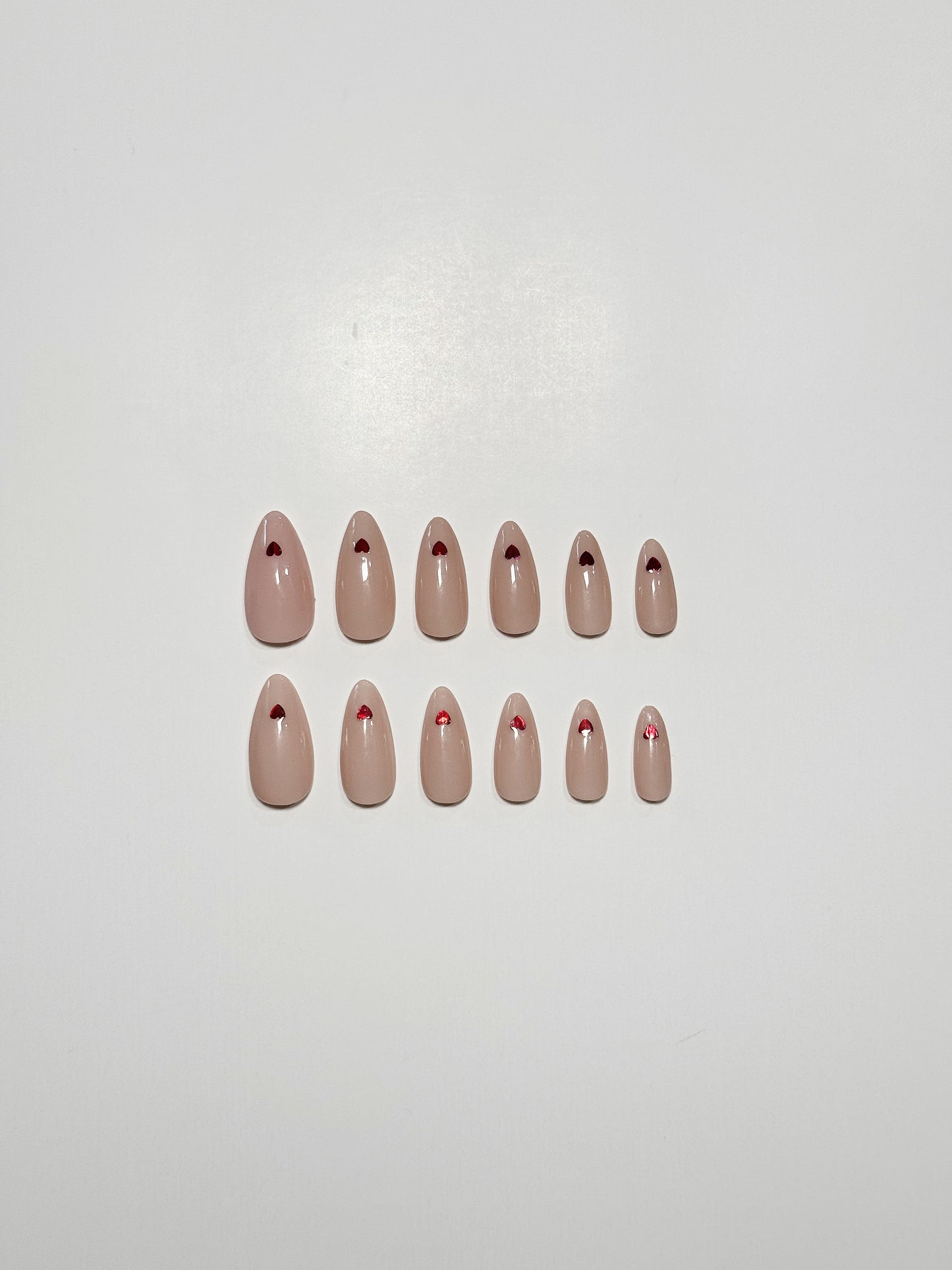 Nude, medium length, almond shaped press on nails with red hearts.