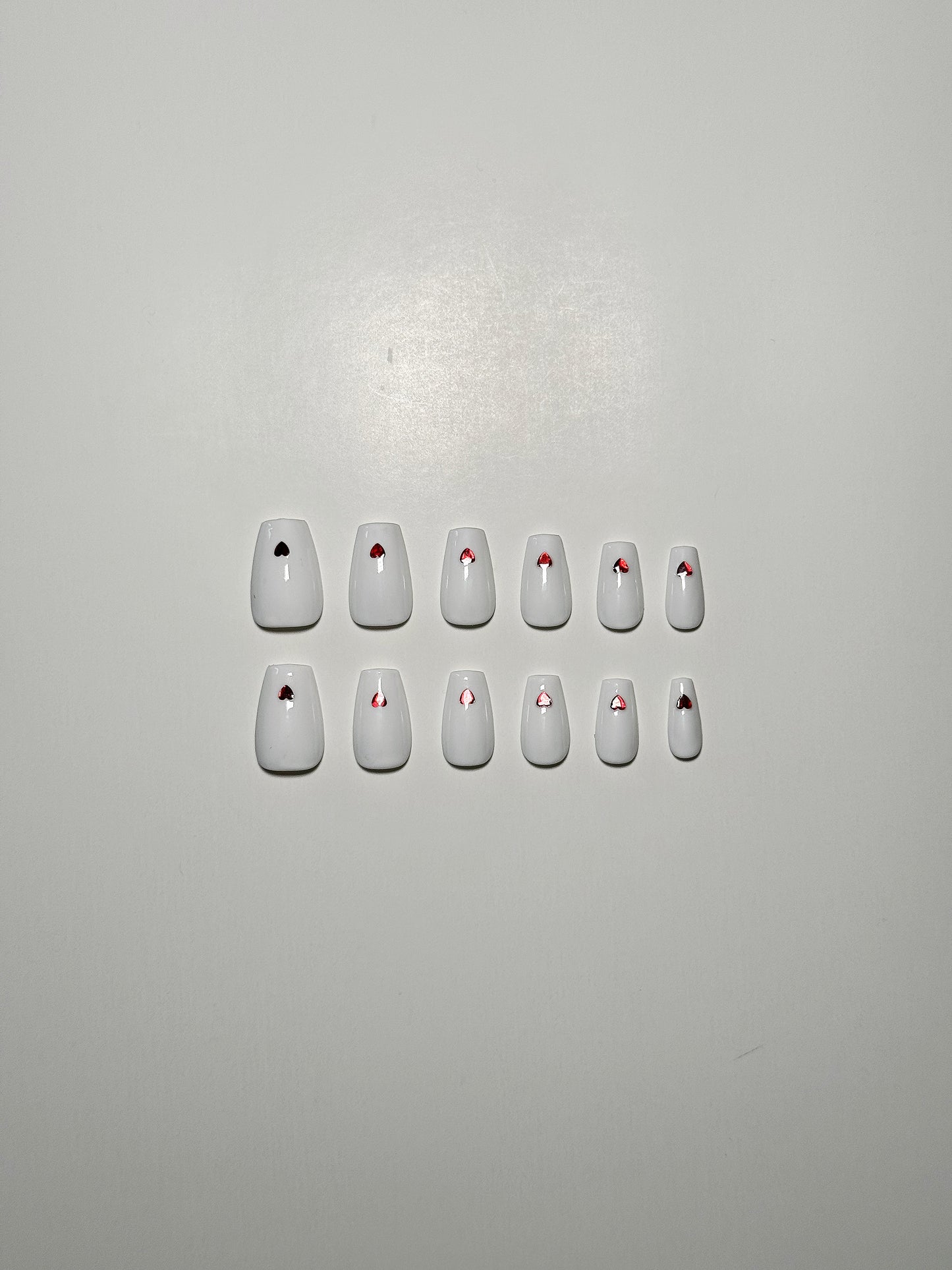 White, medium length, almond shaped press on nails with red hearts.