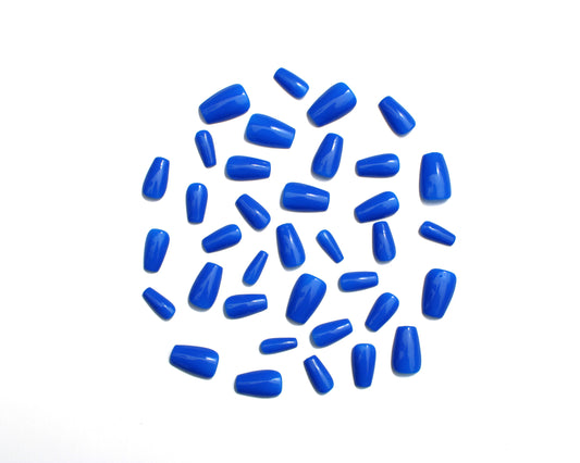 Solid cobalt blue, medium length, coffin shaped, luxury press on nails scattered on a white background.